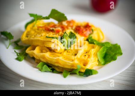 Omelette aux œufs farcie à la tomate et aux légumes verts frits sous forme de gaufres, sur une table en bois. Banque D'Images