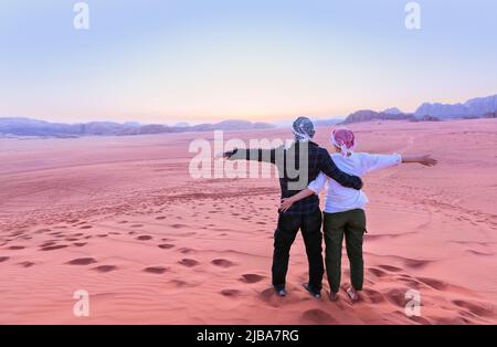 Un jeune couple regarde au lever du soleil sur le rhum wadi Désert en Jordanie Banque D'Images