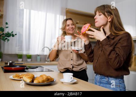 Sa fille apprécie un délicieux donut que sa mère a traité. Femme et fille ayant le thé dans la cuisine Banque D'Images