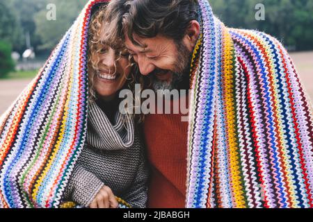 Un couple caucasien adulte plein de joie sous une couverture colorée rient et s'amusent ensemble avec amour et amitié. Jeunes adultes dans les loisirs en plein air r Banque D'Images