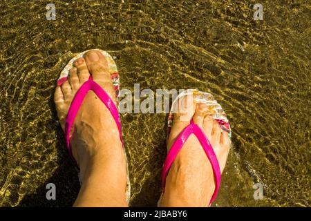 Pieds d'une femme inconnue, portant des tongs, sur la plage en mer Banque D'Images