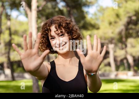 Adorable femme à tête rouge portant des vêtements de sport debout sur le parc de la ville, en plein air montrant et pointant vers le haut avec les doigts numéro dix tout en souriant confiant et Banque D'Images