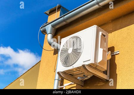 Chaude journée d'été. Refroidissement. Air conditionné suspendu à l'extérieur sur le mur d'un bâtiment ou d'une maison moderne à côté du toit contre un ciel bleu. Banque D'Images
