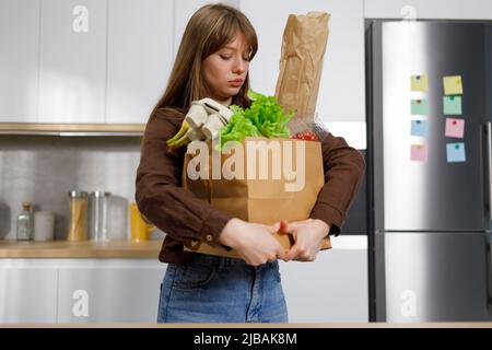 Une jeune femme tient dans ses mains un sac de shopping en papier lourd rempli de légumes et de produits frais. Banque D'Images