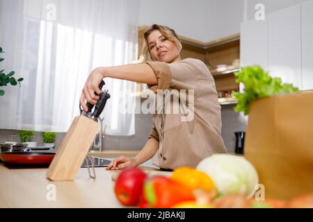 Jolie femme tirant un couteau d'un bloc de bois. Cuisine de la femme de ménage dans la cuisine Banque D'Images
