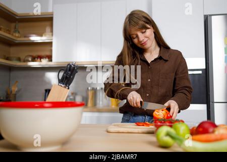 Bonne jeune femme sur la cuisine moderne de couper des légumes. Processus de cuisson Banque D'Images