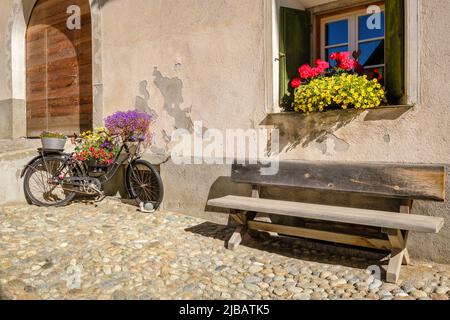 Un vieux vélo rouillé, décoré de belles fleurs, dans le centre historique du village de S-Chanf (haute vallée de l'Engadine , Grisons, Suisse) Banque D'Images