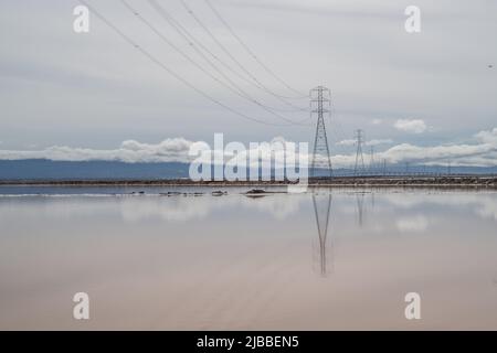 L'eau vitreux de type miroir des étangs d'évaporation de sel reflétant les nuages et les lignes électriques. Banque D'Images