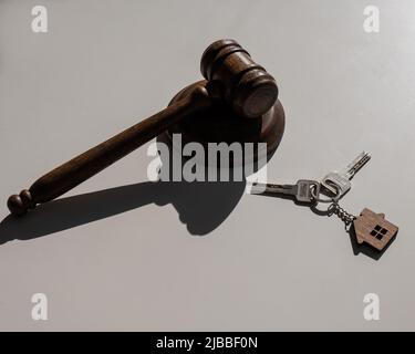 Des clés avec porte-clés en forme de maison et un gavel de juge sur fond blanc. Banque D'Images