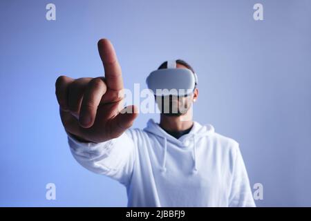 Jeune homme touchant un bouton dans un espace virtuel. Jeune homme qui interagit avec le métaverse à l'aide d'un casque de réalité virtuelle. Homme qui vit un simulati de 3D ans Banque D'Images