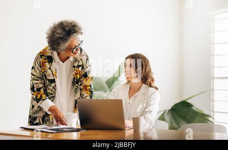 Une femme directrice discutant avec son collègue dans une salle de réunion. Deux femmes d'affaires diverses collaborant à une nouvelle tâche dans une startu appartenant à une femme Banque D'Images