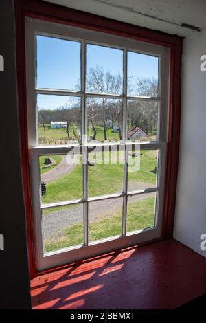 Village colonial américain rural et bâtiments vus à travers une ancienne fenêtre rouge de Pennsylvanie à 12 panneaux avec lumière du soleil à l'intérieur. Espace de copie, non Banque D'Images