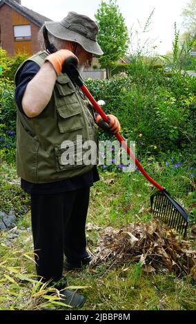 Un homme âgé travaille dans le jardin. Râteler les feuilles tombées ensemble. Il porte un chapeau pour se protéger des rayons du soleil Banque D'Images