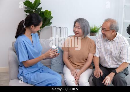 Jeune infirmière prenant soin des personnes âgées assises sur un canapé. Une femme qui aide les patients âgés tout en souriant. Banque D'Images