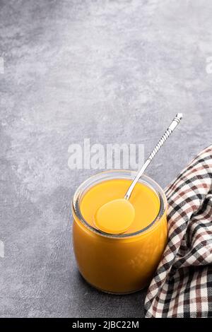 Purée de fruits jaune et orange dans un pot en verre sur fond gris Banque D'Images