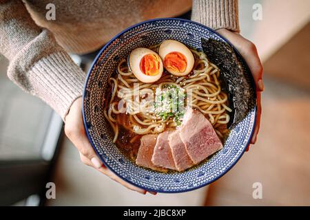 Mains tenant un bol de soupe de nouilles ramen japonaises Banque D'Images