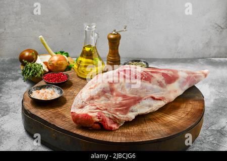 Chump de jambe d'agneau cru avec des ingrédients sur une souche en bois Banque D'Images