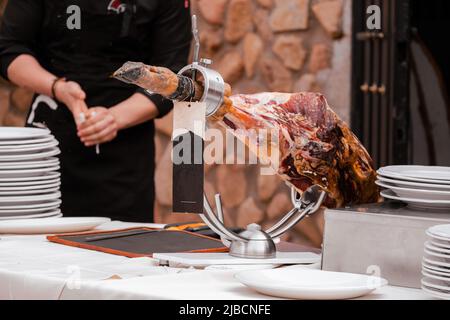 Un jambon ibérique sur une table de restauration pour un événement à côté du cutter professionnel préparant les ustensiles Banque D'Images