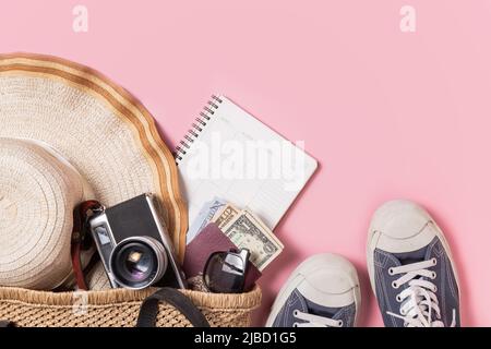 Accessoires de voyage, chapeau de plage avec appareil photo rétro, lunettes de soleil, argent et passeport dans un sac en maille fait main avec sneaker sur fond rose pastel Banque D'Images