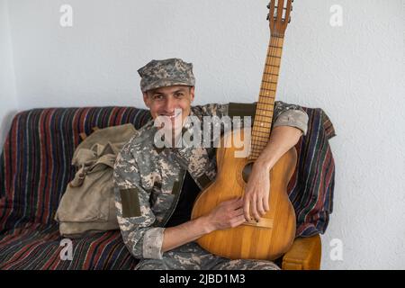 Vétéran du concept de jeu de guitare en fauteuil roulant. Réunion de famille. Fils et femme. Uniforme de camouflage. Contexte familial. Se reposer ensemble. Des sentiments qui se manifestent Banque D'Images