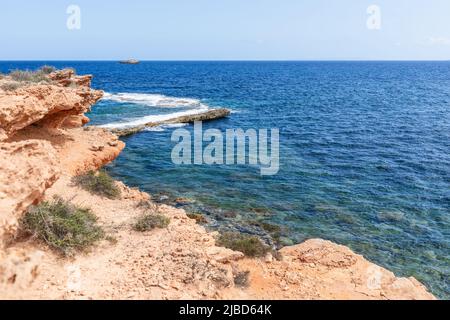 Côte rocheuse rose-orange avec plantes rares, l'eau change de couleur selon la profondeur, ciel clair, jour d'été, Ibiza, Iles Baléares, Espagne Banque D'Images