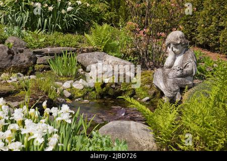 Petite statue sur le bord de l'étang avec Trillium grandiflorum blanc - fleurs de la Trinité dans le jardin d'arrière-cour au printemps. Banque D'Images