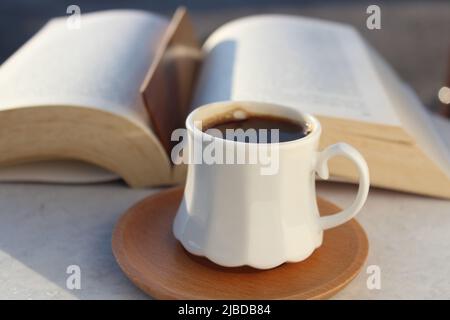 Lire un livre sur le balcon de la maison au coucher du soleil avec une tasse de café turc. Signet en bois à l'intérieur du livre. Ambiance de détente, activité culturelle. Liberté, information, concept de connaissance. Banque D'Images