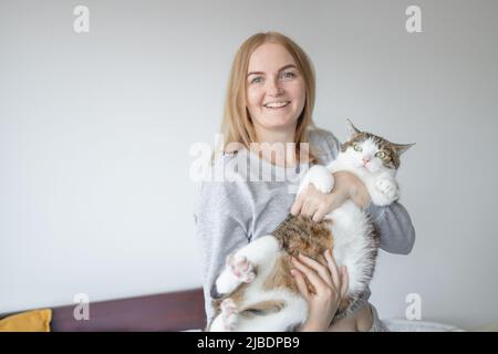 Portrait d'une jeune blonde 30s femme tenant un chat gris mignon avec des yeux verts. Femme embrassant son adorable chaton. Banque D'Images
