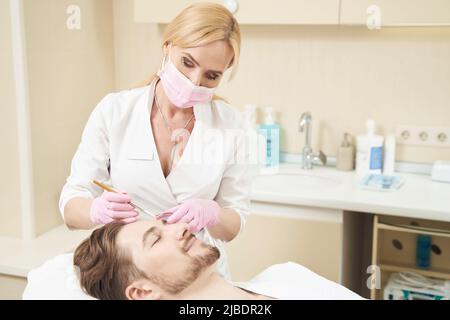 Femme spécialiste en cosmétologie appliquant un liquide chimique sur le visage du patient Banque D'Images