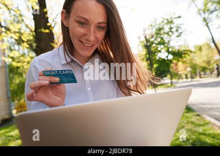 Jolly jeune femme faisant des paiements à l'aide d'un ordinateur portable à l'extérieur Banque D'Images