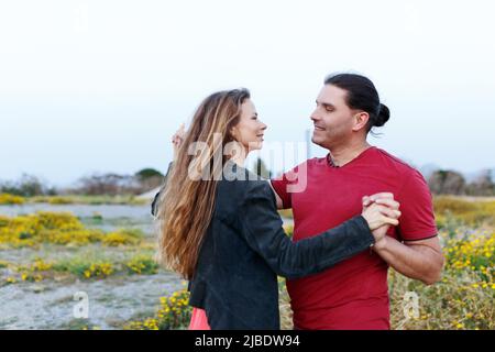 Portrait d'un charmant couple d'âge moyen qui regarde l'un sur l'autre et qui s'embrasse tout en dansant sur l'herbe dans le parc d'été. Banque D'Images