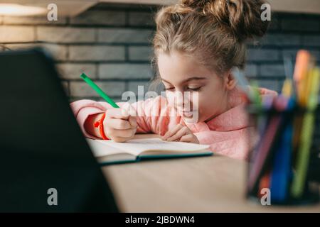 Écolière e-learning, faire des devoirs à écrire dans le copybook, avoir videocall conférence conversation avec le professeur sur tablette numérique. Éducation Banque D'Images