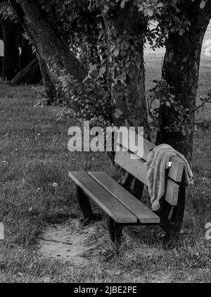 Une photo minimaliste d'un banc solitaire dans un parc, avec un pull laissé sur lui, donnant un sentiment d'abandon - photographie de stock Banque D'Images