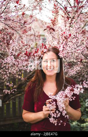 Bonne femme debout parmi les branches de l'arbre à fleurs au printemps. Banque D'Images