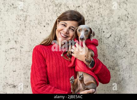 Femme latine tenant son chien, vêtu de rouge et regardant l'appareil photo Banque D'Images