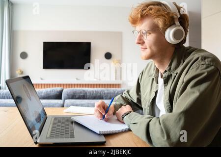 Un jeune homme irlandais au gingembre dans un casque d'écoute d'un coach professionnel lors d'un séminaire en ligne Banque D'Images