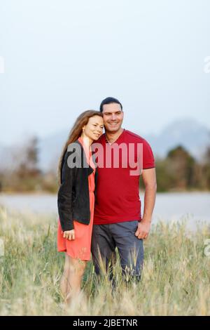 Portrait d'un charmant couple d'âge moyen regardant à côté de l'espace d'imitation et s'embrassant tout en étant debout sur l'herbe dans le champ d'été. Banque D'Images