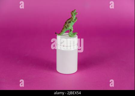 Flacon blanc et dinosaure miniature sur fond violet. Petite figure verte d'un animal de proie debout sur ses pattes arrière. Cylin plastique fermé Banque D'Images