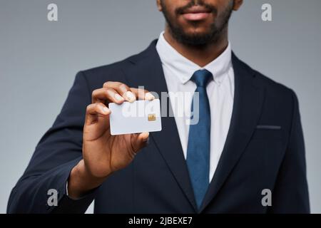 Gros plan d'un homme d'affaires noir tenant une maquette de carte de crédit vierge et montrant à l'appareil photo, espace de copie Banque D'Images