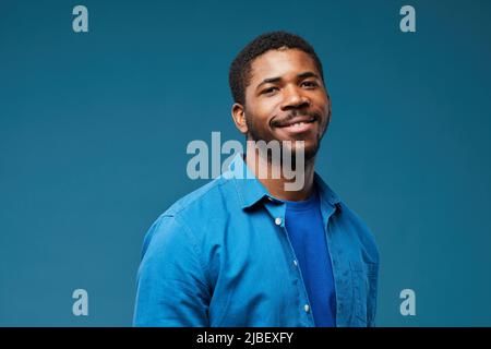 Portrait d'un homme afro-américain souriant portant le bleu sur fond bleu et regardant l'appareil photo, l'espace de copie Banque D'Images