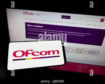 Personne possédant un smartphone avec le logo de l'Office of Communications (Ofcom) de l'autorité britannique sur l'écran devant le site Web. Mise au point sur l'affichage du téléphone. Banque D'Images