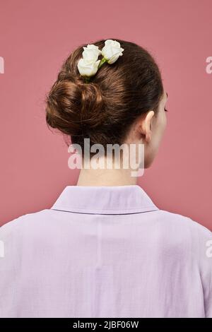 Vue arrière minimale d'une jeune femme avec des roses dans les cheveux sur fond rose vif Banque D'Images