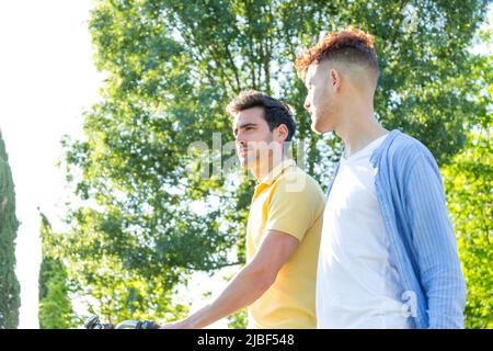 Un jeune couple de mâles qui profite d'une promenade ensemble lors d'une journée ensoleillée en plein air dans le parc. LGBT et concept de relation. Banque D'Images