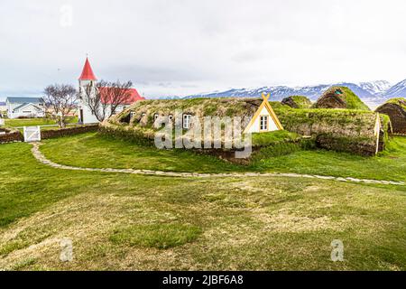 Les maisons en tourbe du musée en plein air de Glaumbær près de Varmahlíð, Skagafjörður, Islande, s'alignent avec des toits recouverts d'herbe et une entrée en gâble encadrée de jaune. L'église paroissiale blanche avec son clocher rouge et son toit se dresse en arrière-plan. Les 13 bâtiments en tourbe avec six pignons orientés vers l'avant étaient habités jusqu'en 1947. Glaumbær est un musée depuis 1948. L'église a été reconstruite dans sa forme actuelle en 1926, ses panneaux muraux provenant d'une chaire fabriquée en 1685. Banque D'Images