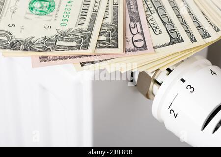 Pile de billets de banque en dollars sur la batterie du radiateur de chauffage avec thermostat. Concept de coûts de chauffage coûteux et de facture énergétique croissante Banque D'Images