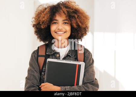 Gros plan d'un étudiant souriant avec un manuel et un ordinateur portable debout regardant l'appareil photo Banque D'Images