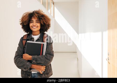 Portrait d'un étudiant souriant tenant un ordinateur portable et un ordinateur portable dans un couloir Banque D'Images