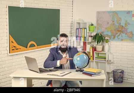 Meilleure éducation possible ici. Un élève de sexe masculin s'assoit dans une salle de classe avec carte. Examen réussi. Apprentissage du sujet. Géographe. Homme heureux avec barbe regarder Banque D'Images