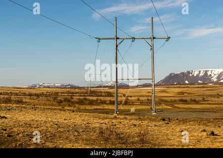 Un pylône électrique avec deux pylônes plus petits derrière lui se dresse sur un plateau près du lac Mývatn dans le nord de l'Islande, devant des montagnes tabulaires enneigées baignées par la lumière du soir. La ligne traverse la municipalité de Þingeyjarsveit le long de la route Kísilvegur. Banque D'Images