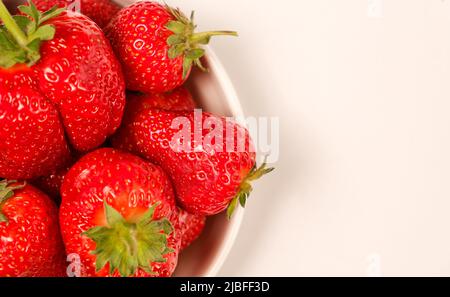 Fraises rouges juteuses dans une assiette sur fond blanc avec espace pour le texte, vue rapprochée du dessus. Banque D'Images